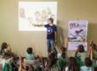 José Aguiar ministra oficina de quadrinhos para crianças com projeção e banner da Malu ao fundo